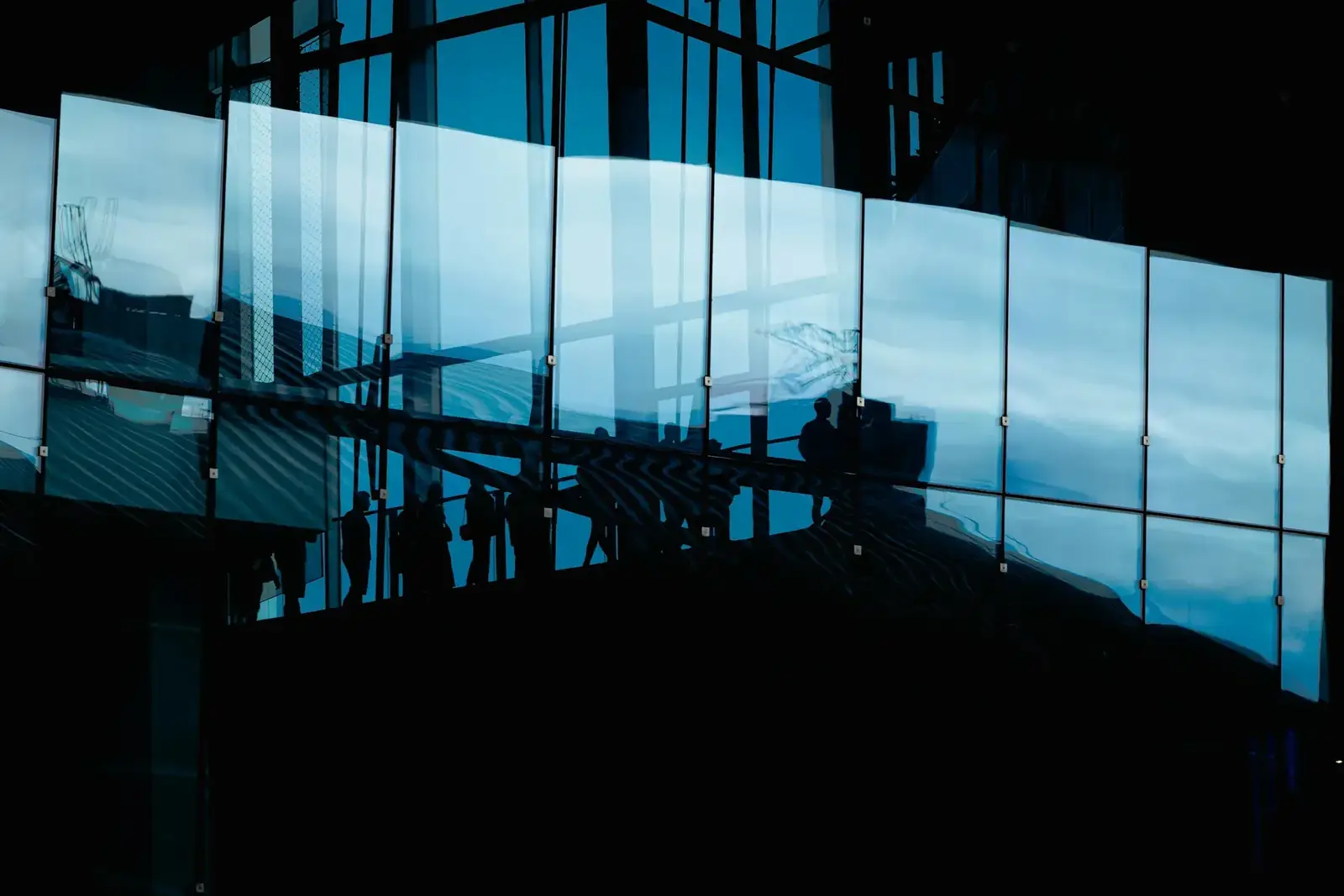 The blue glass facade of a modern building with a team silhouetted inside, the kind of structure and team Lumex is built around