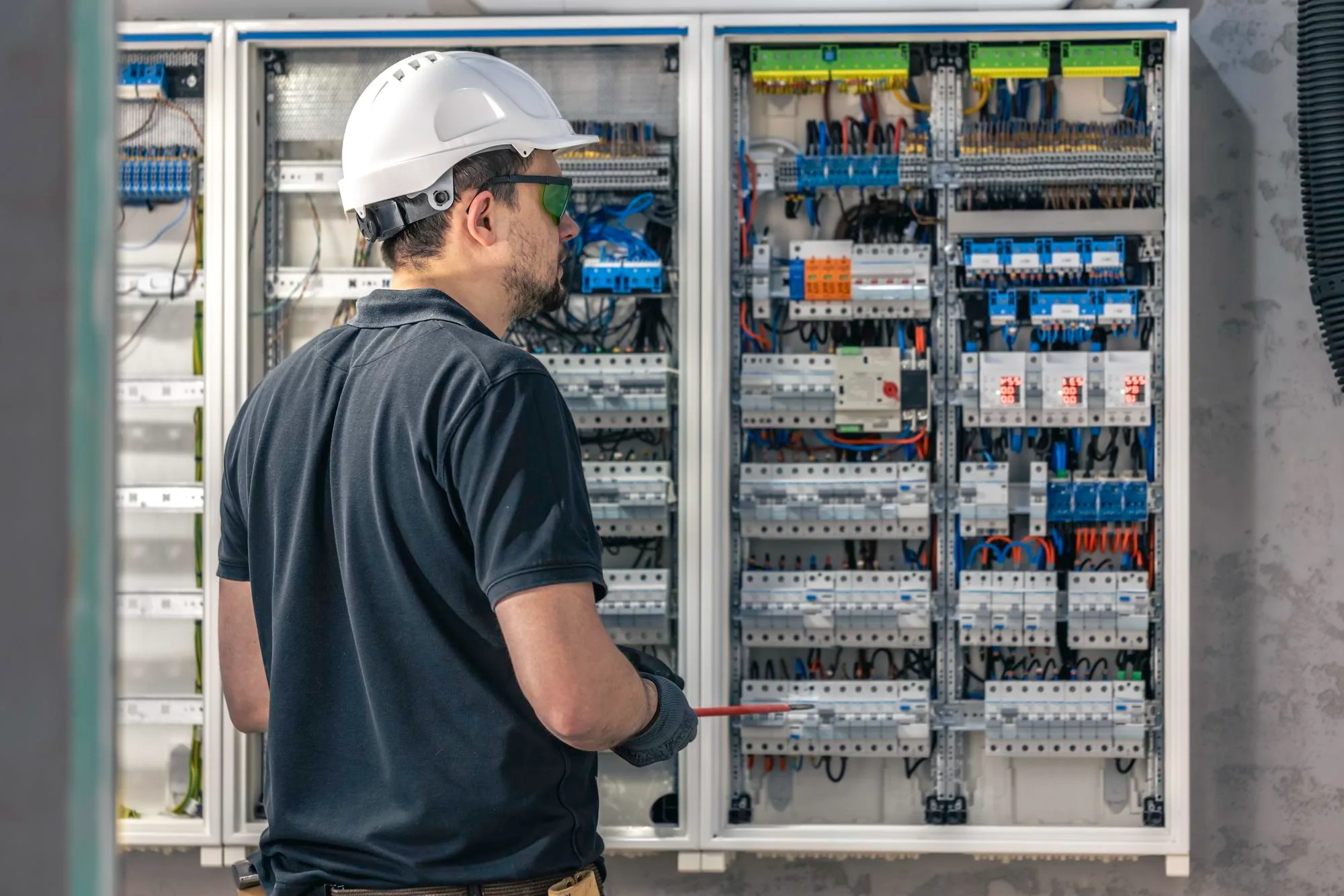Electrician in a hard hat and safety glasses inspecting a low-voltage distribution board, illustrating the critical infrastructure an IEC 62305 lightning risk assessment protects