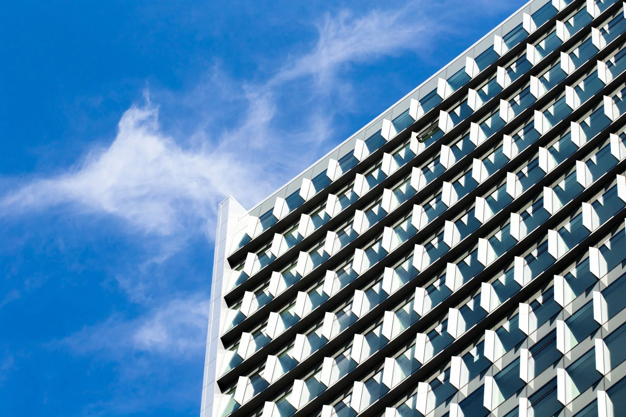 The geometric glass and aluminium facade of a high-rise against a blue sky, the kind of structure an IEC 62305 risk assessment protects