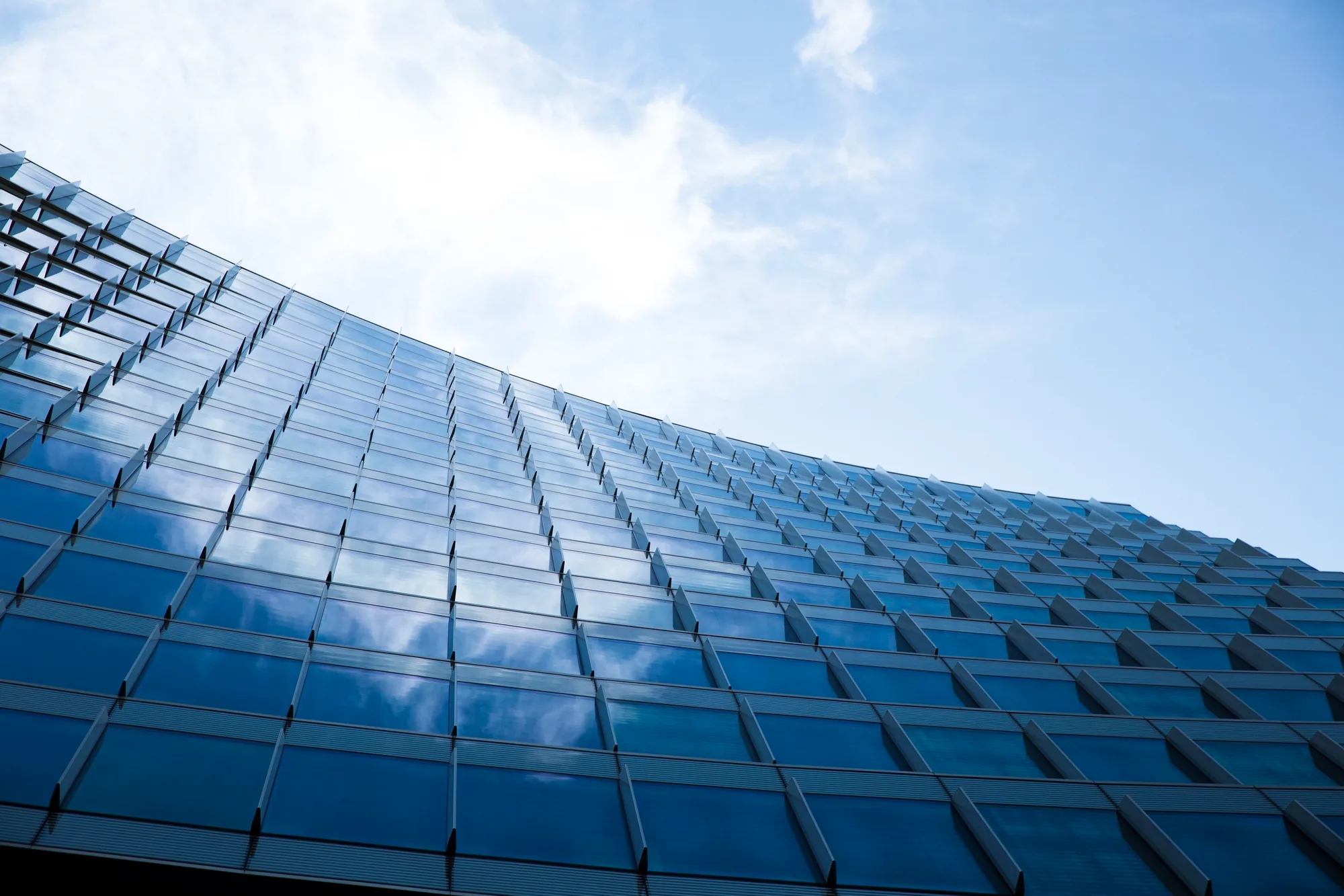 The curved glass facade of a modern high-rise reflecting blue sky and clouds, the kind of structure an IEC 62305 risk assessment protects